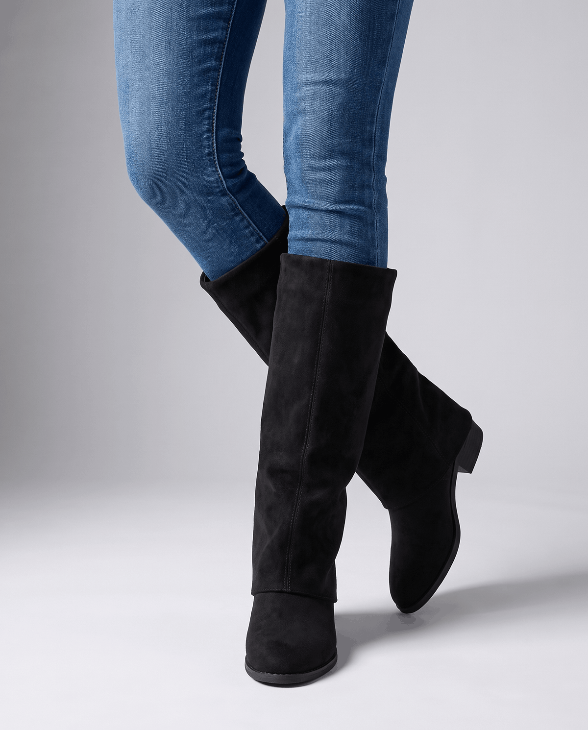 Black fold-over boots worn standing with light-wash jeans tucked in