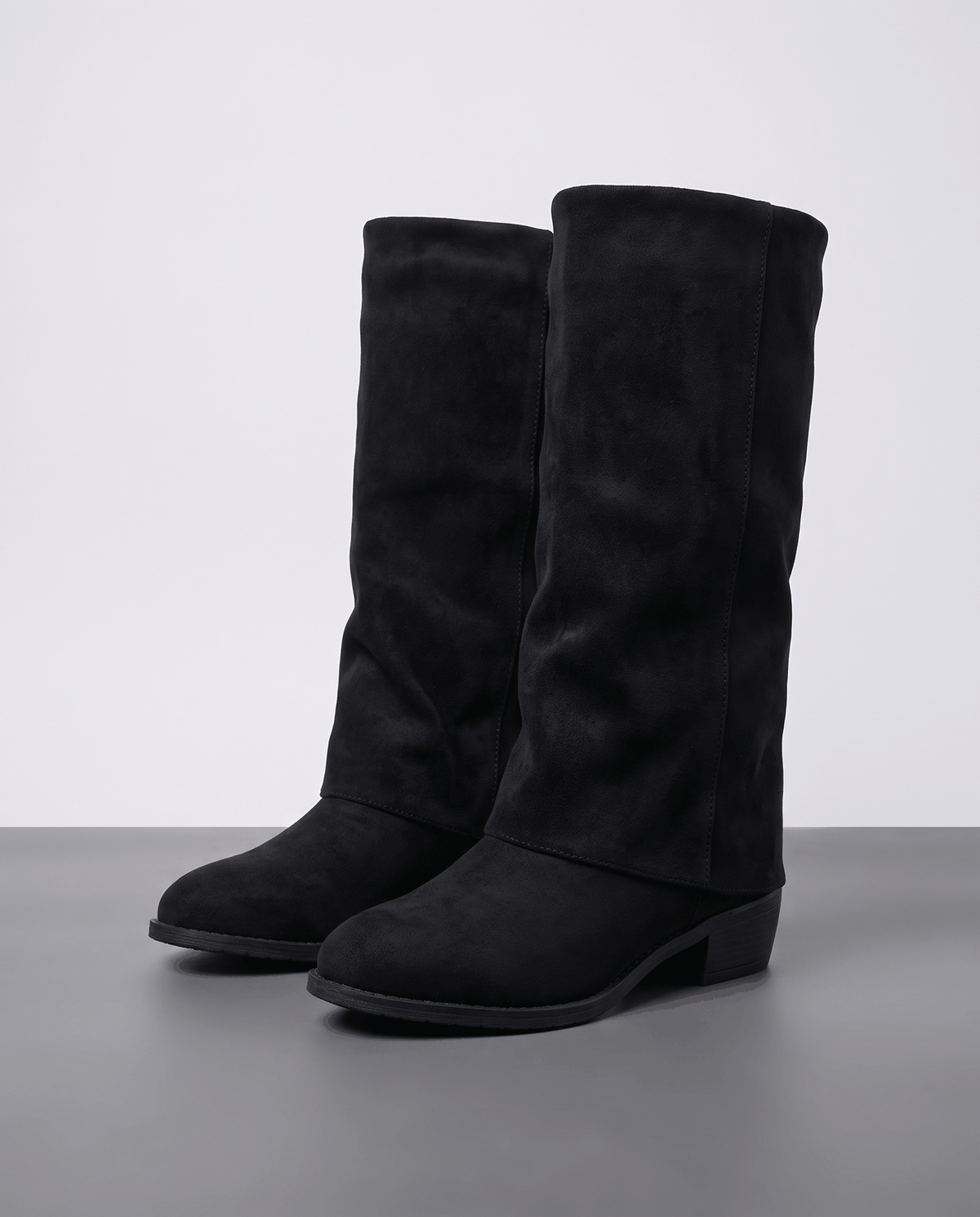 Pair of black fold-over vegan suede boots on a grey studio floor