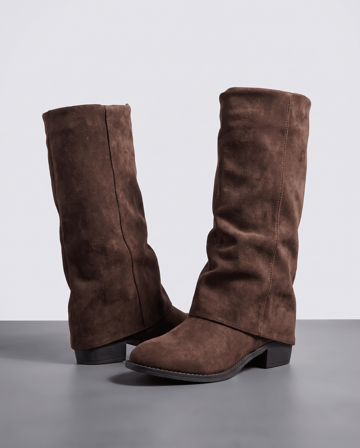 Brown slouchy suede boots standing on a grey studio floor, angled view