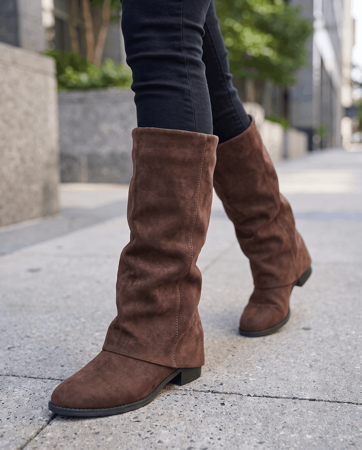 Brown suede boots worn walking on a city sidewalk with black leggings