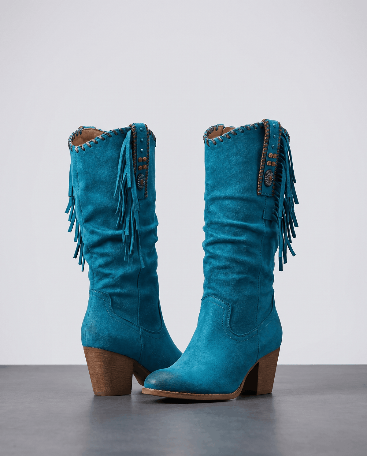 Pair of blue slouchy fringe boots with turquoise-bead straps on a grey floor