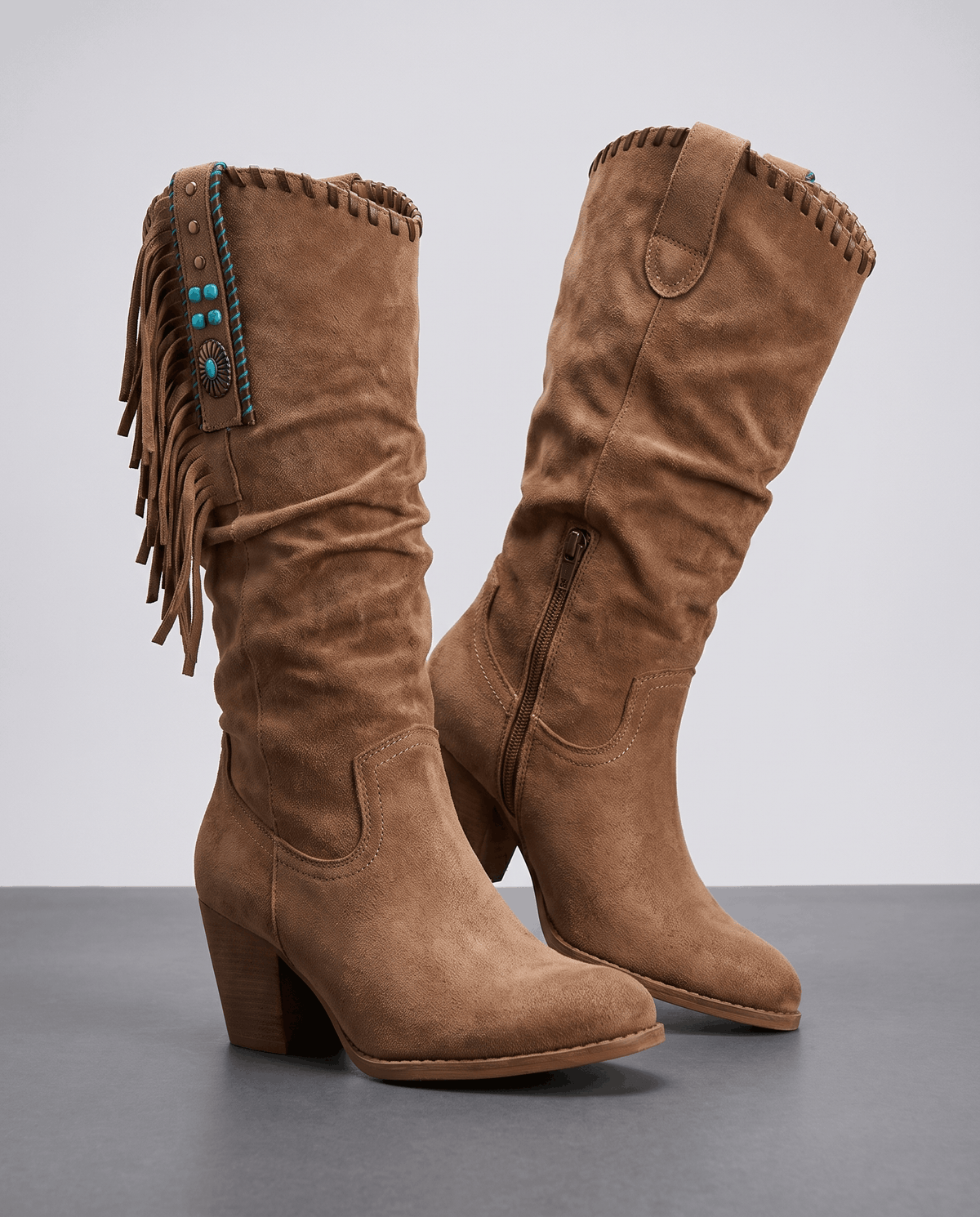Pair of brown slouchy western boots with side fringe on a grey studio floor