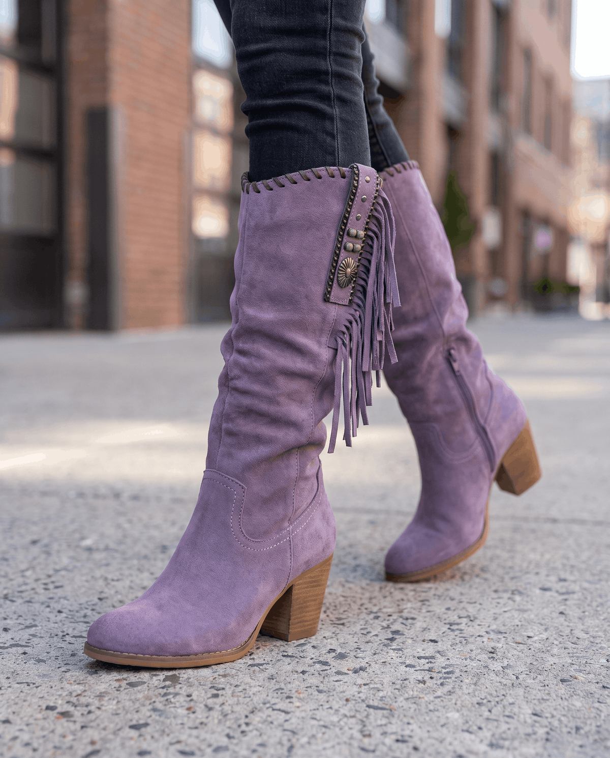 Purple slouchy boots mid-stride on a city sidewalk with dark tucked jeans