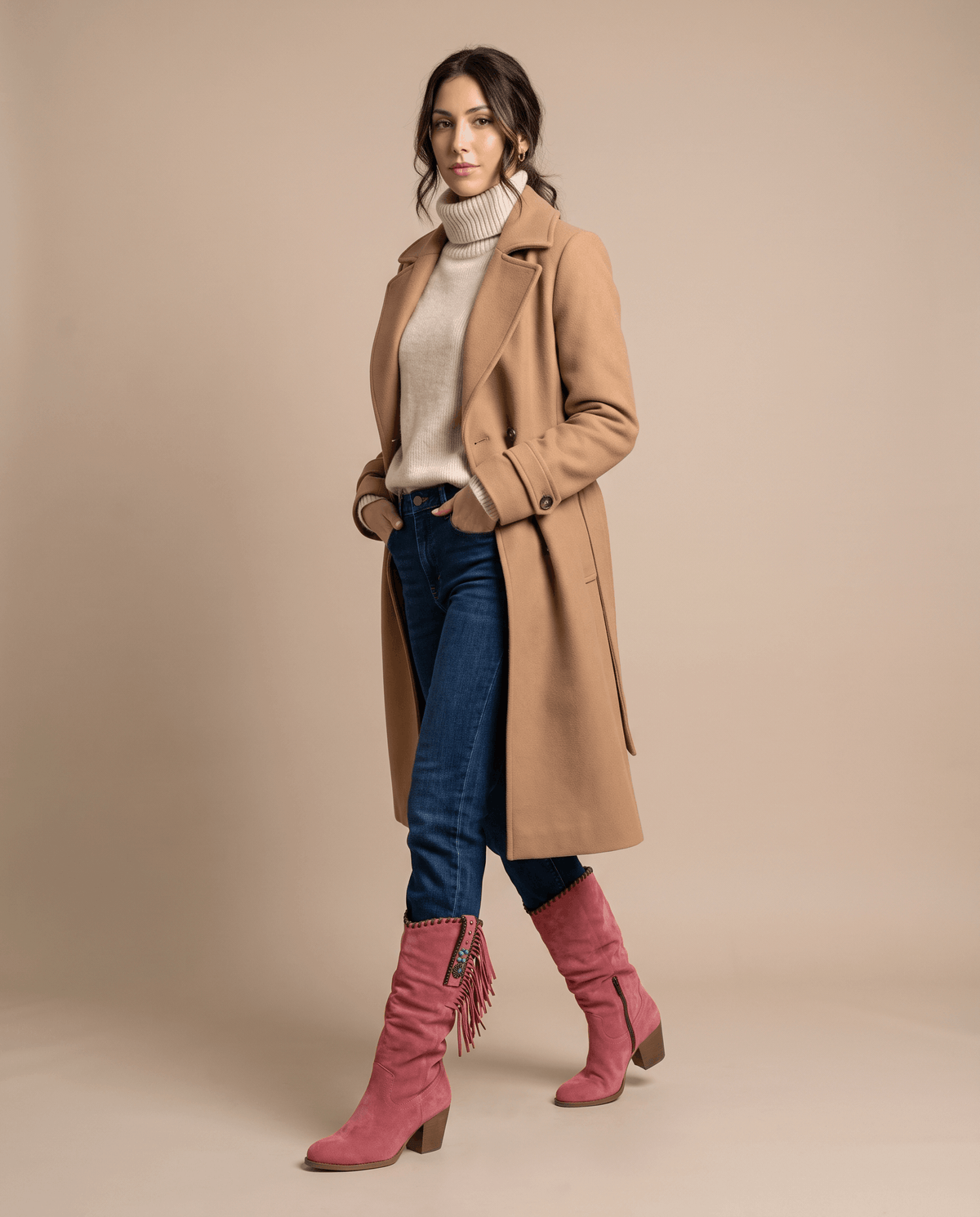 Woman in a camel coat, cream turtleneck and tucked jeans wearing red fringe boots