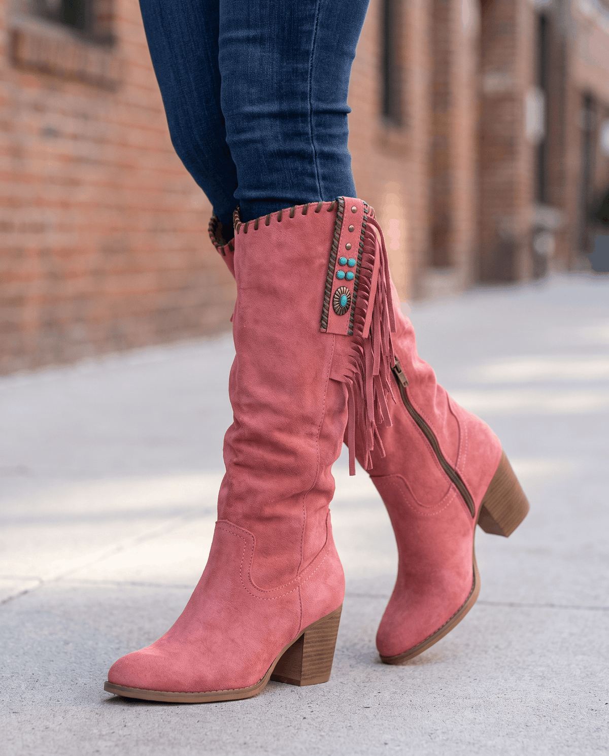 Red western boots with side fringe worn walking on a city sidewalk with jeans