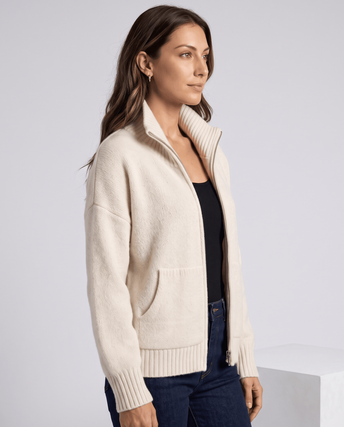 Three-quarter view of a cream zip cardigan worn with a navy top and jeans