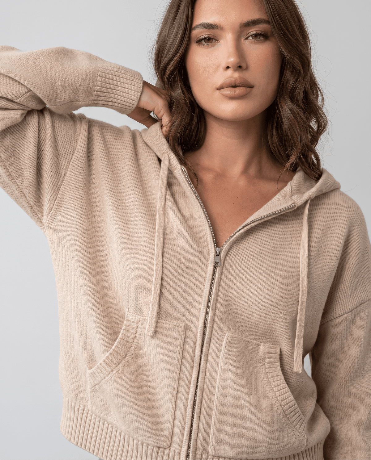 Close-up of beige cardigan zip front and ribbed hem with a hand at the hood