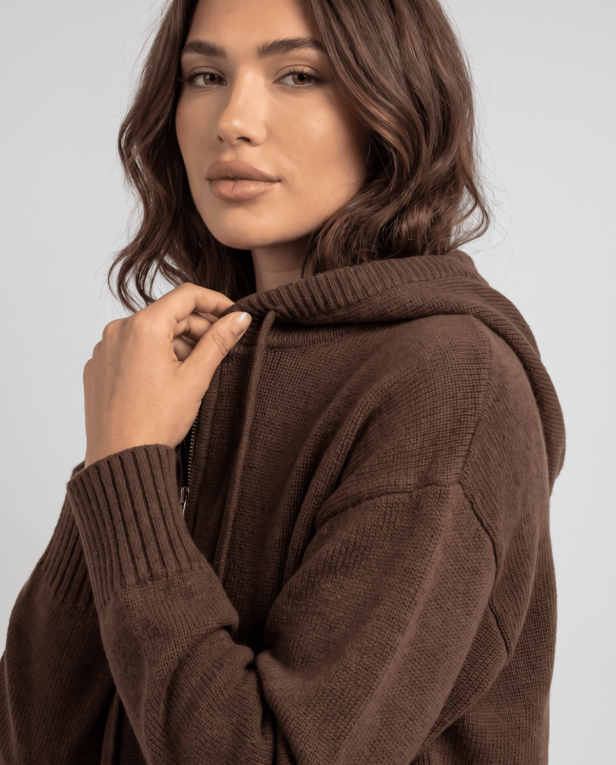 Close-up of dark brown cardigan hood with a hand at the collar and ribbed cuff