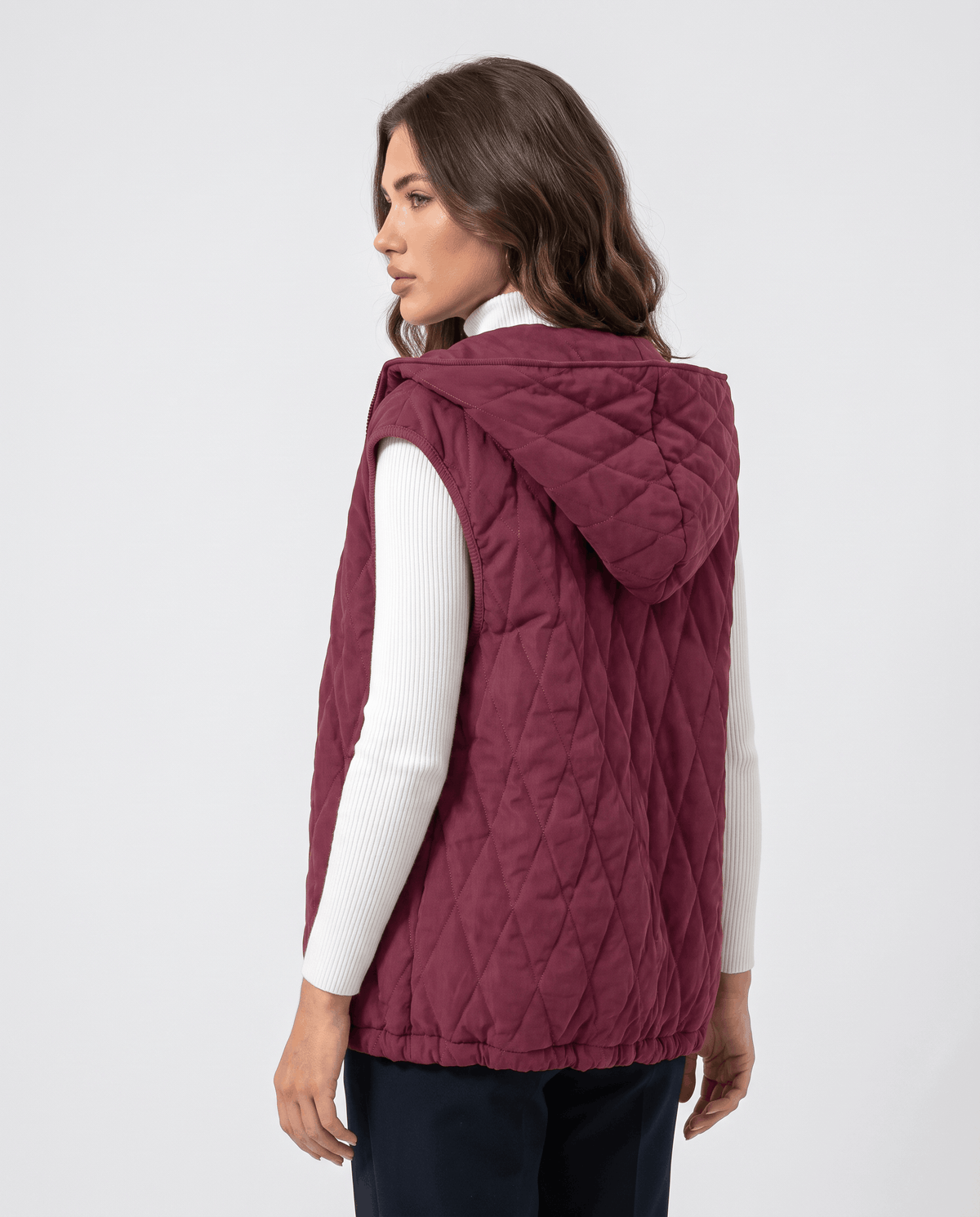 Back view of burgundy hooded quilted puffer vest on a model