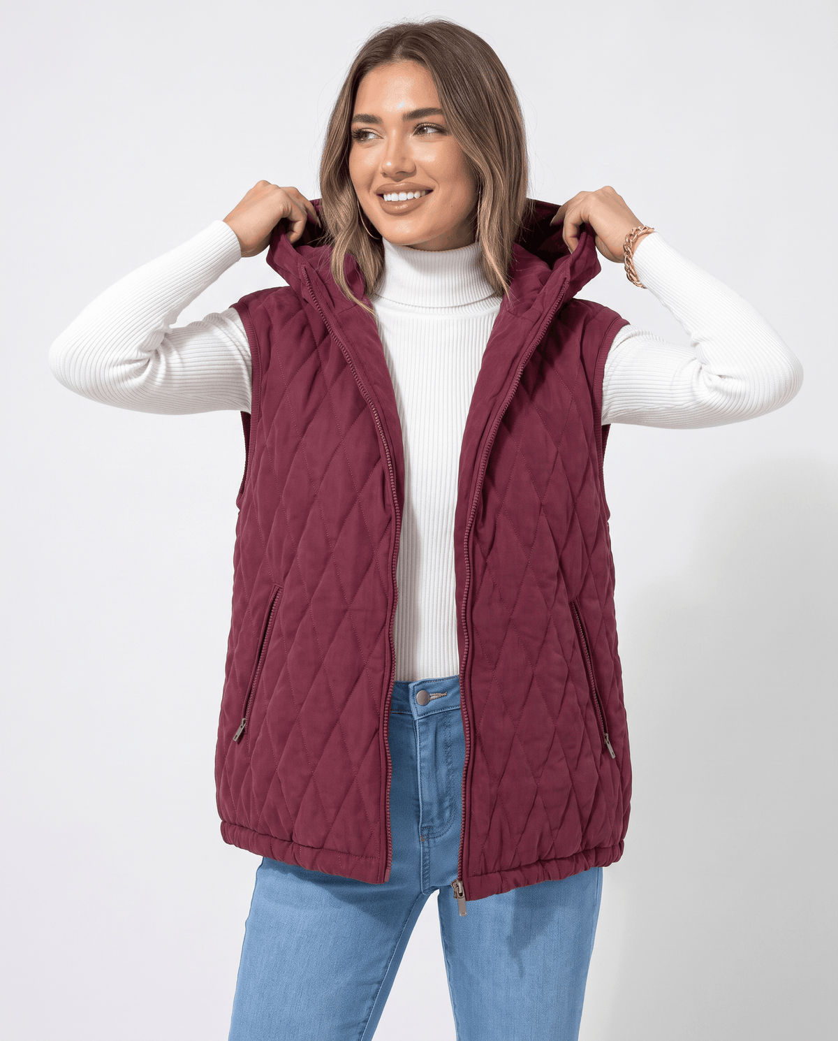 Women's hooded puffer vest in burgundy with oversized fit worn over a white turtleneck