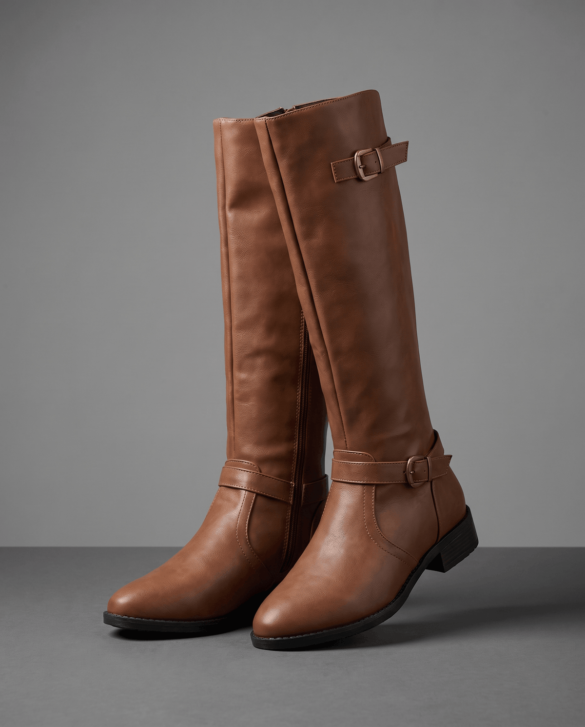 Brown knee-high riding boots with antique brass buckles, a structured shaft, pointed toe, and stacked block heel.
