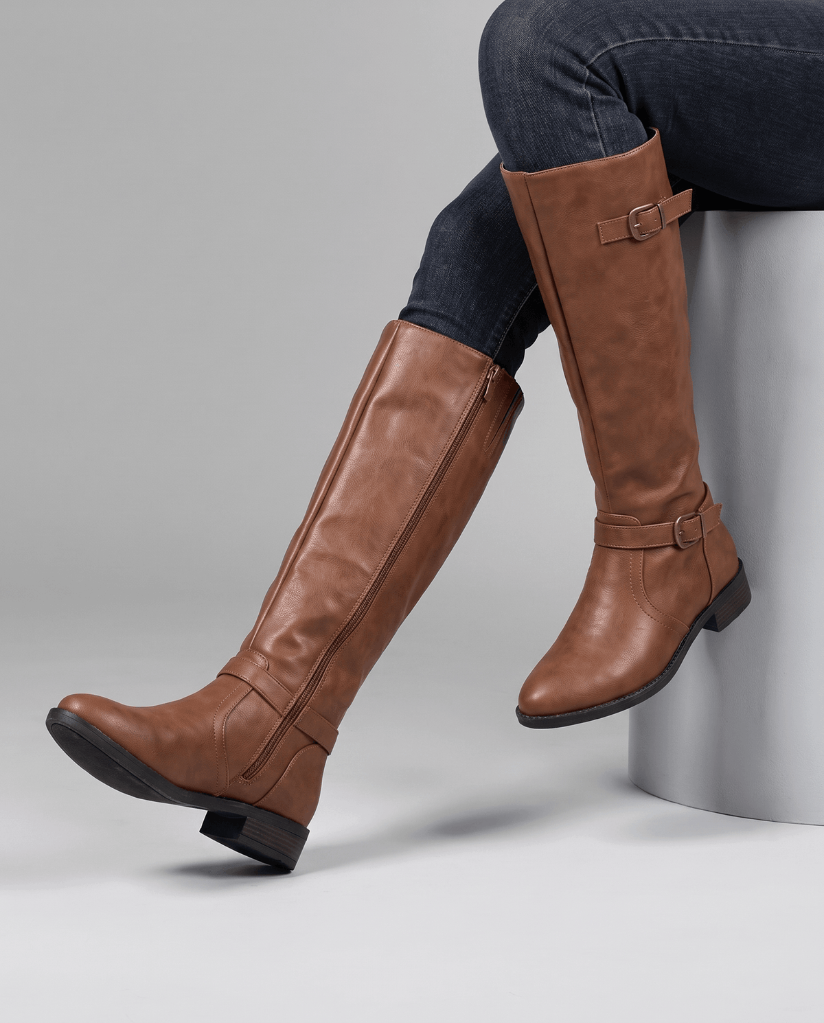 Brown knee-high riding boots with antique brass buckle straps, structured shaft, inside zip, and a stacked block heel.