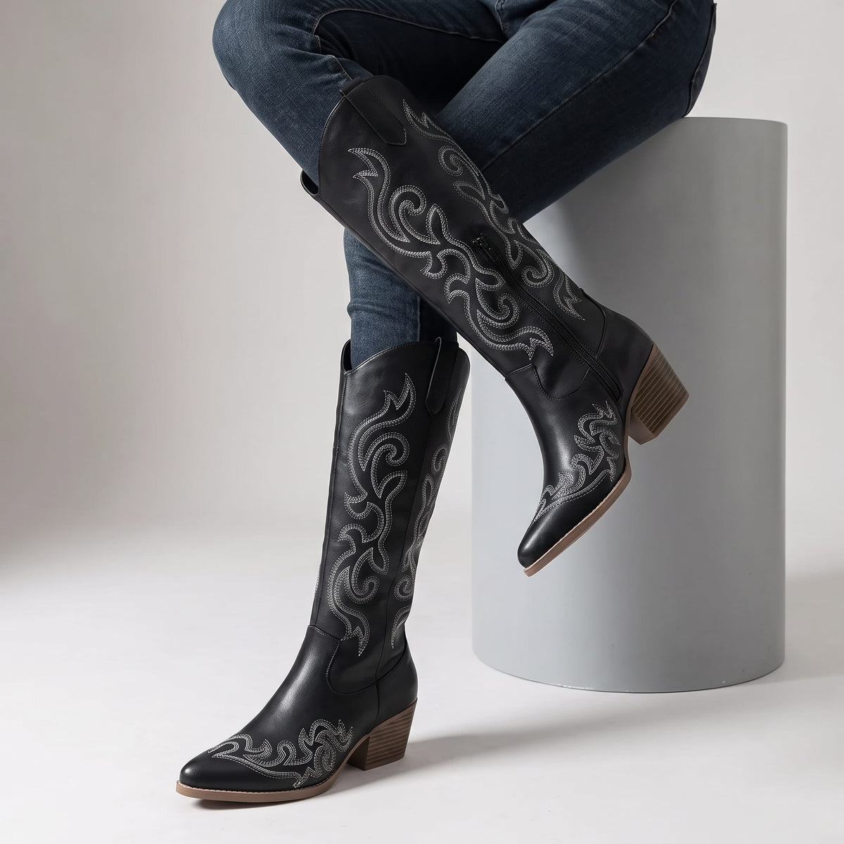 Seated woman in dark jeans with crossed legs wearing black western boots