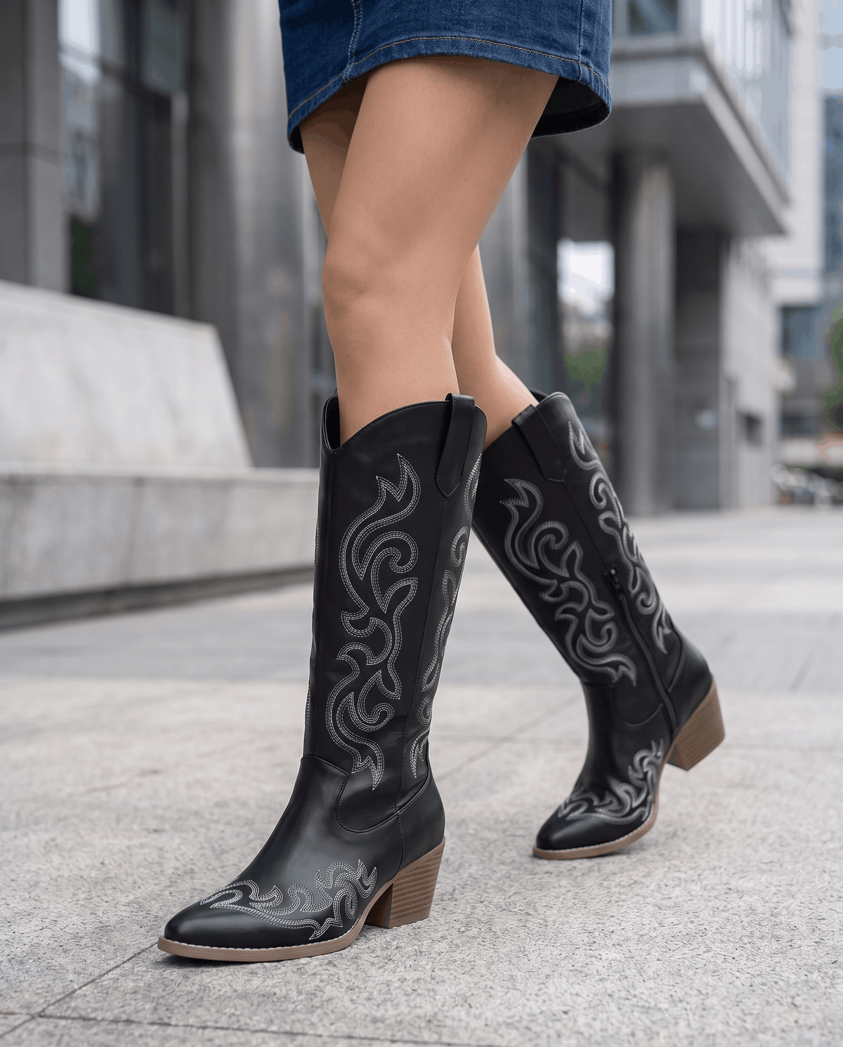Woman in a denim mini skirt walking in black cowboy boots on a sidewalk