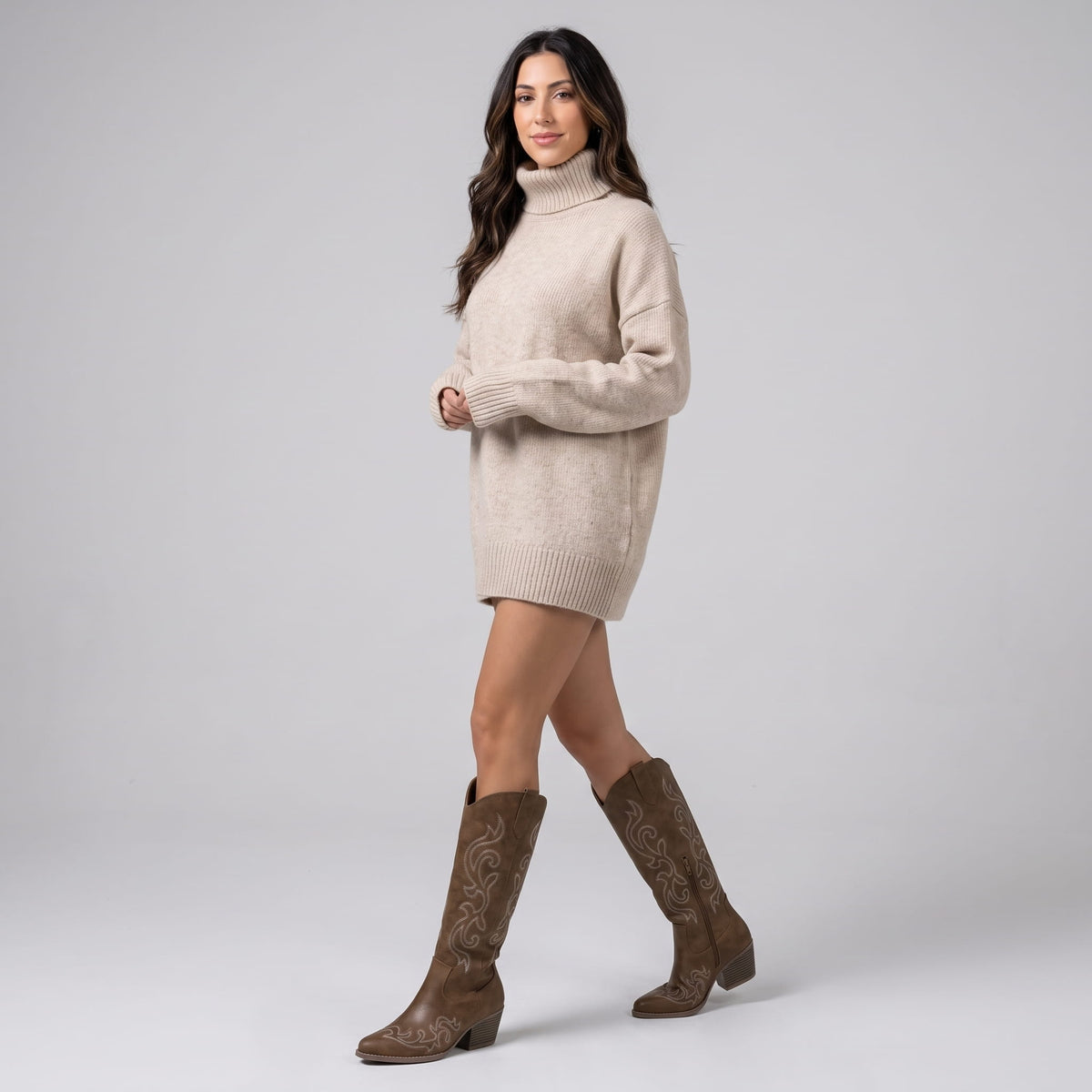 Woman in a cream sweater dress walking in brown cowboy boots