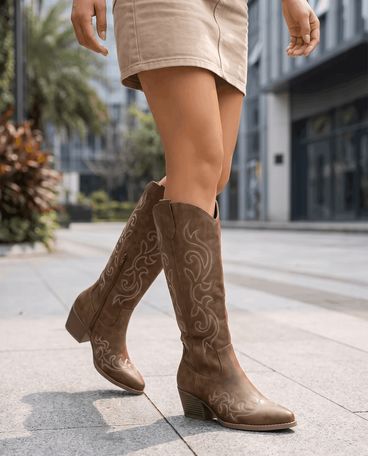 Woman in a beige mini skirt walking on a sidewalk in brown cowboy boots