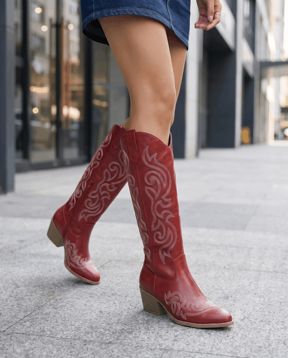 Woman in a denim mini skirt walking on a city sidewalk in red cowboy boots