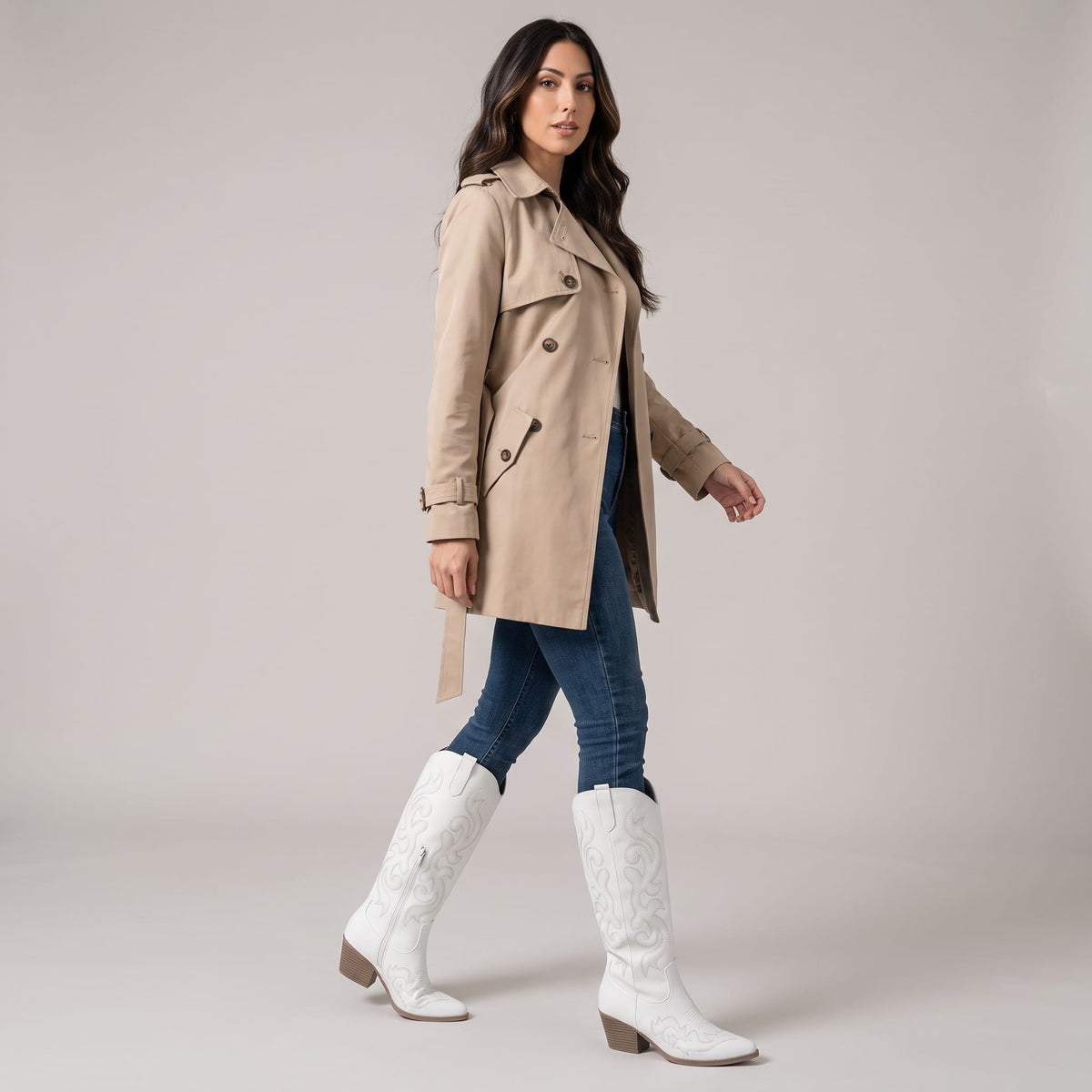 Woman in a beige trench coat and jeans wearing white cowboy boots