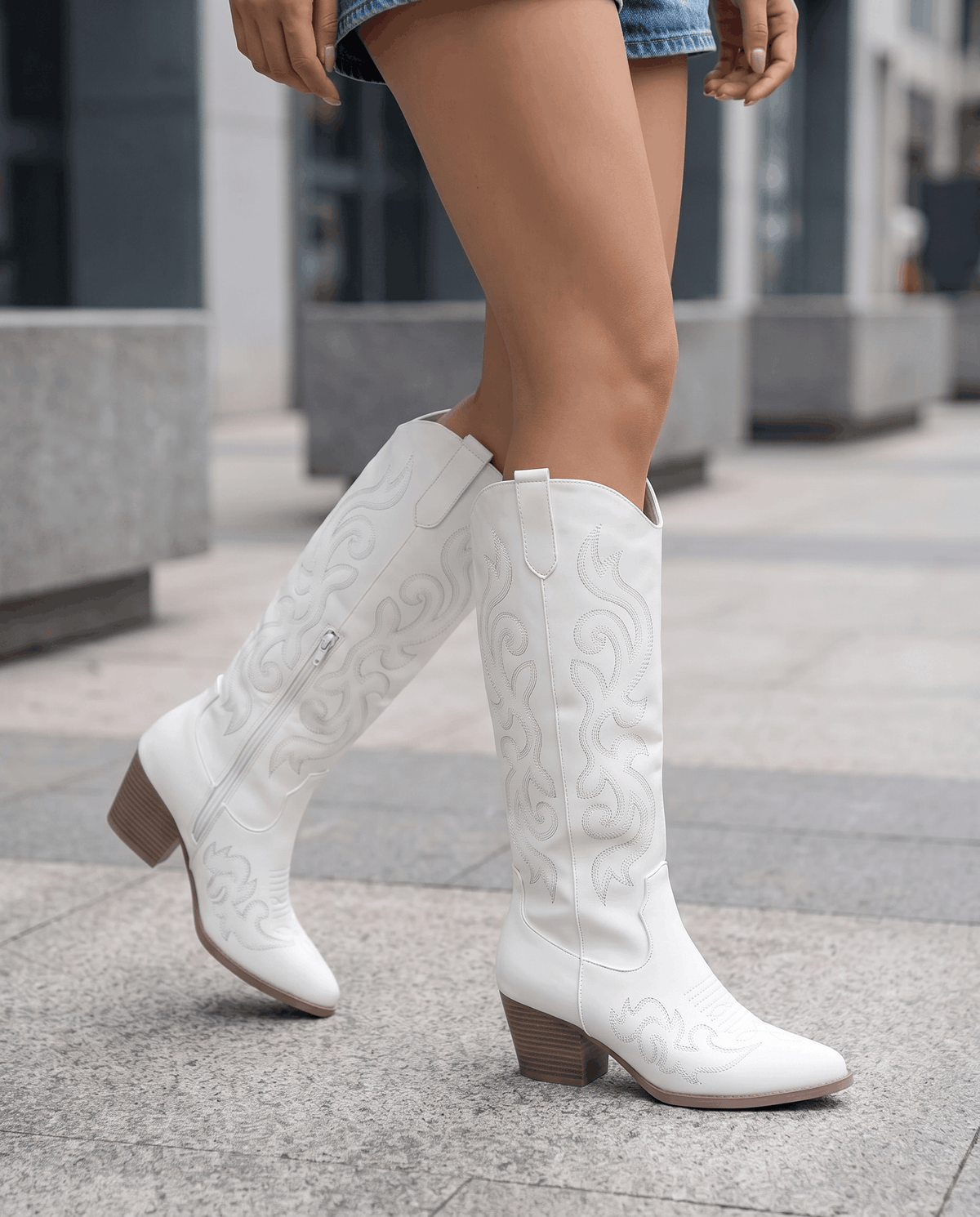Woman in denim shorts walking on a city sidewalk in white cowboy boots