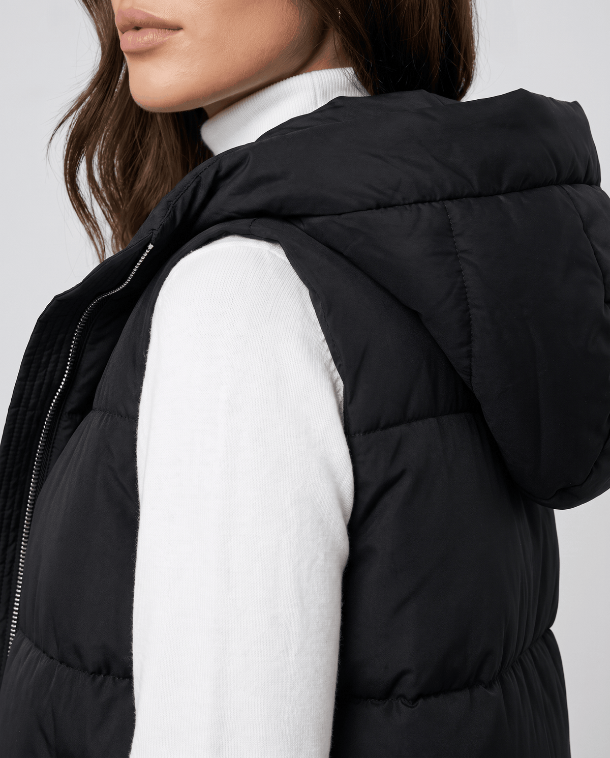 Side detail of black quilted vest hood and sleeveless armhole