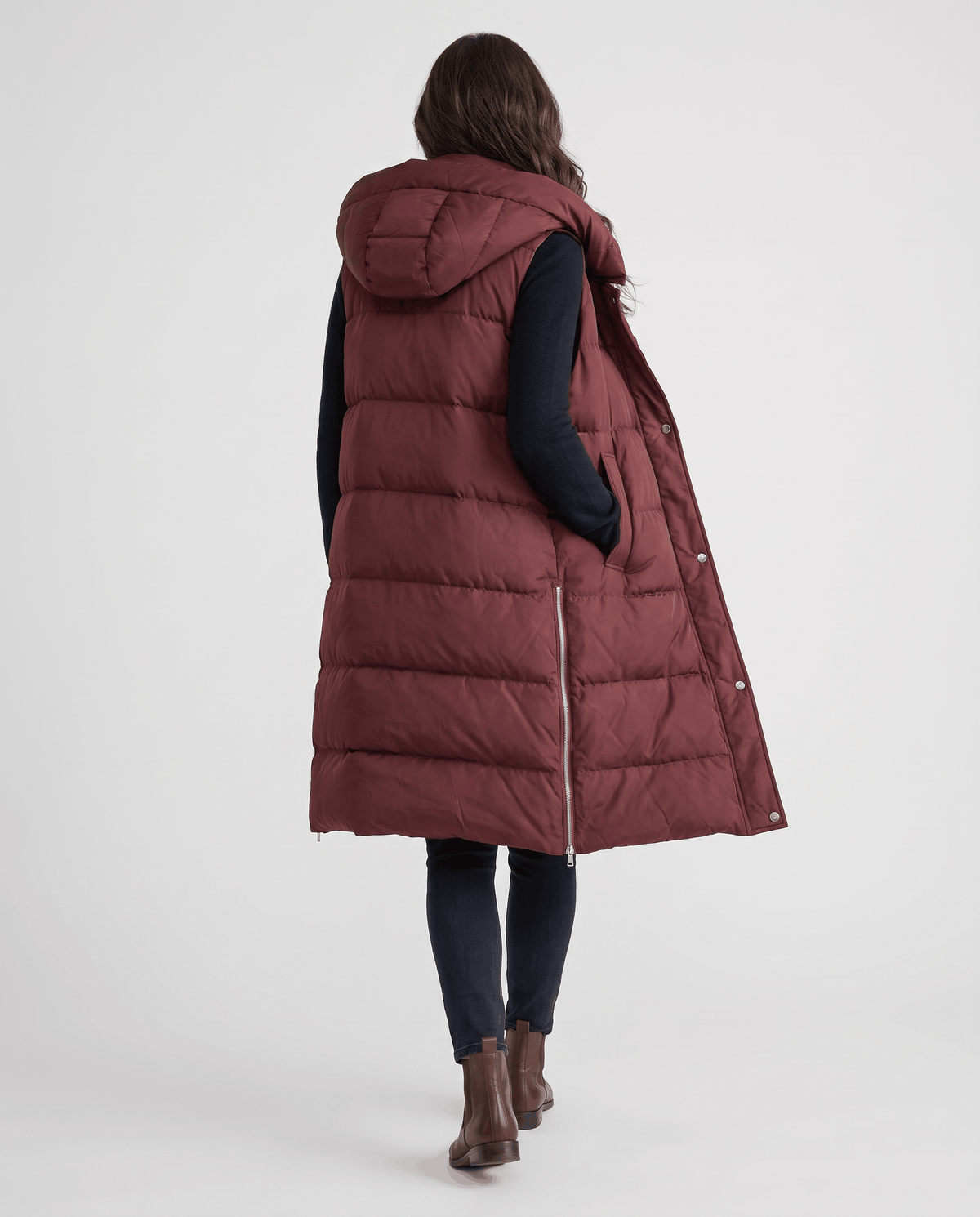 Back view of burgundy knee-length hooded quilted vest on a model