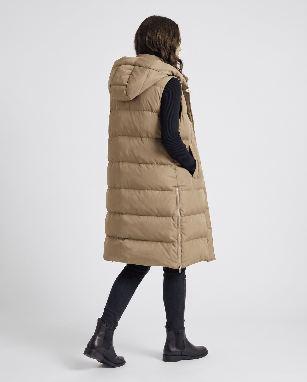 Back view of khaki knee-length hooded quilted vest while walking in boots