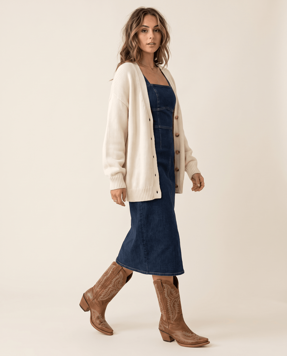 Woman in a cream cardigan and denim midi dress walking in brown western boots