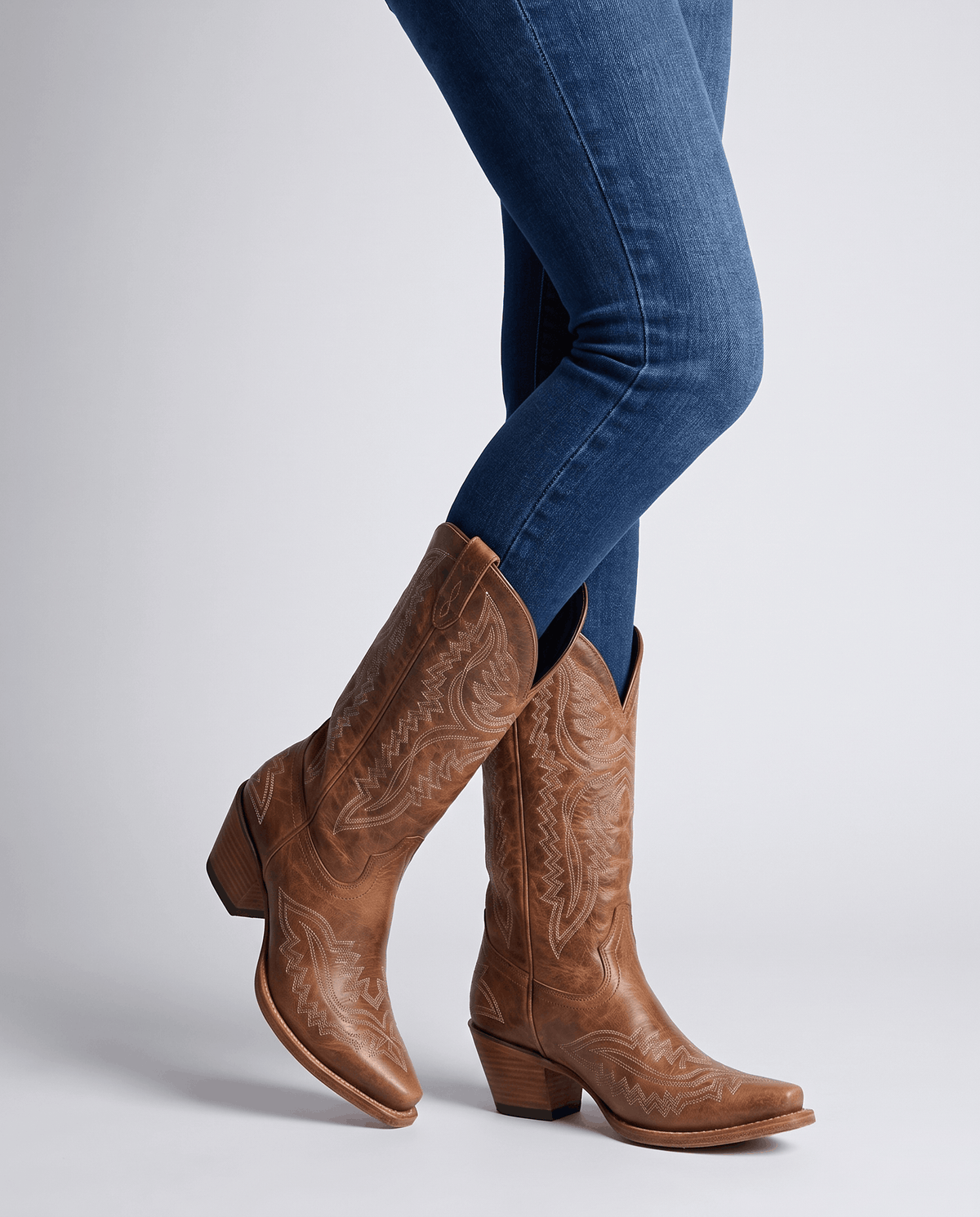 Brown mid-calf boots worn standing with blue jeans tucked into the shaft