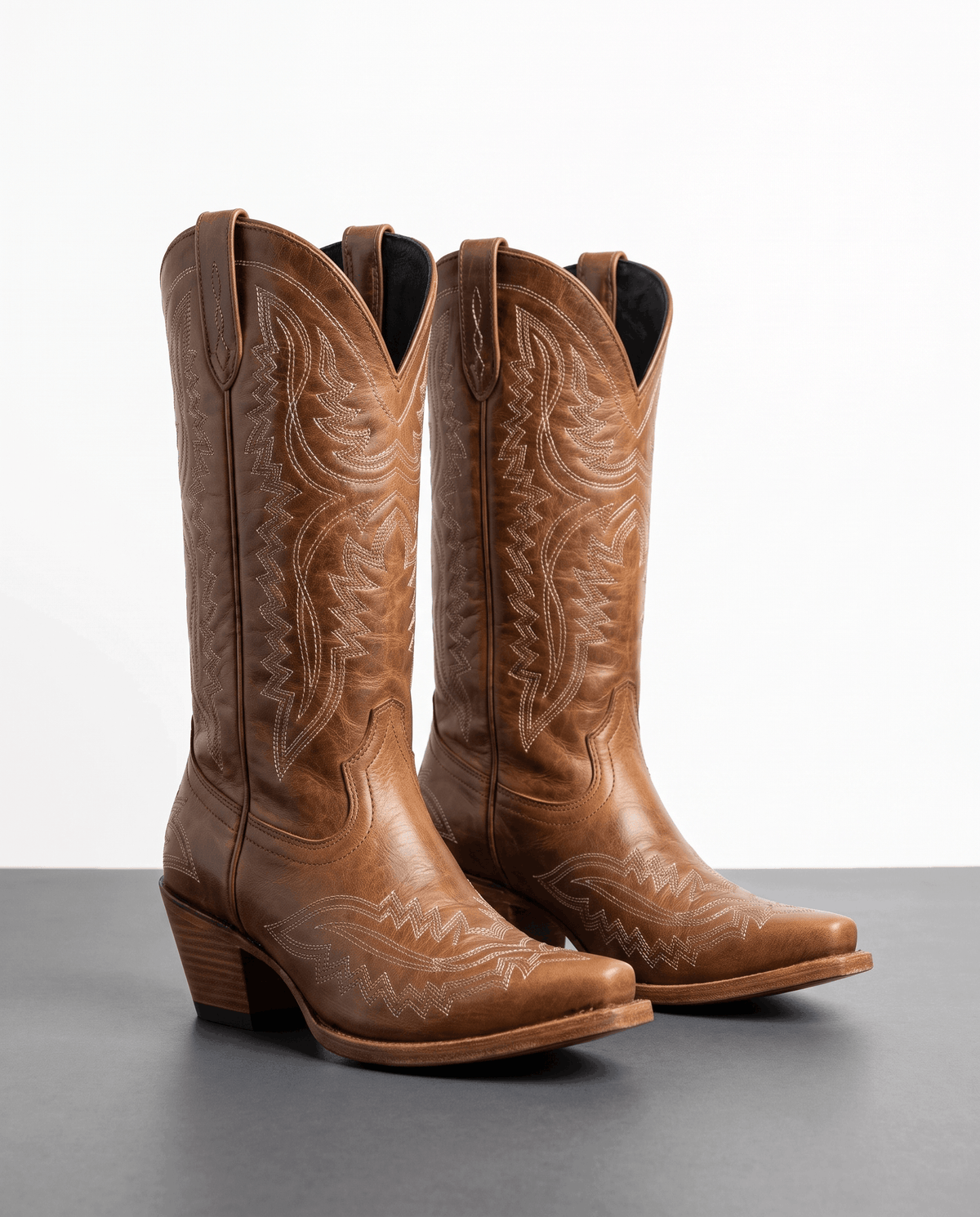Pair of brown embroidered western boots with pointed toes against a light grey backdrop
