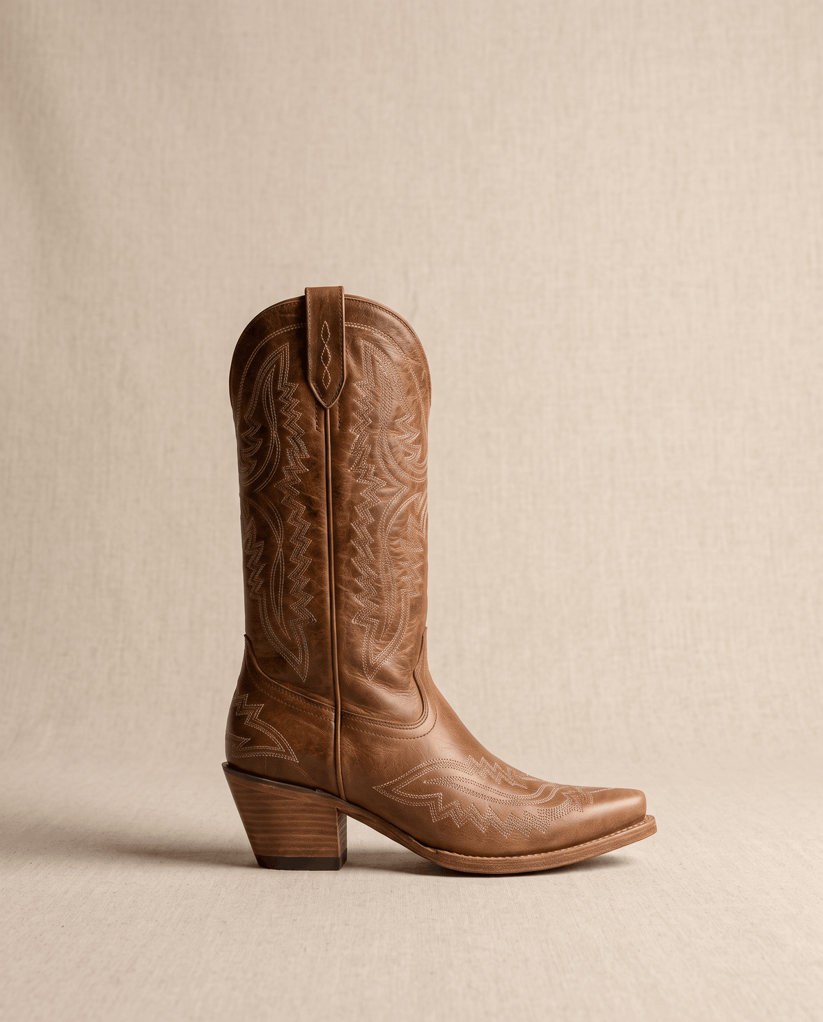 Single brown cowboy boot in side profile with scalloped top and stacked heel