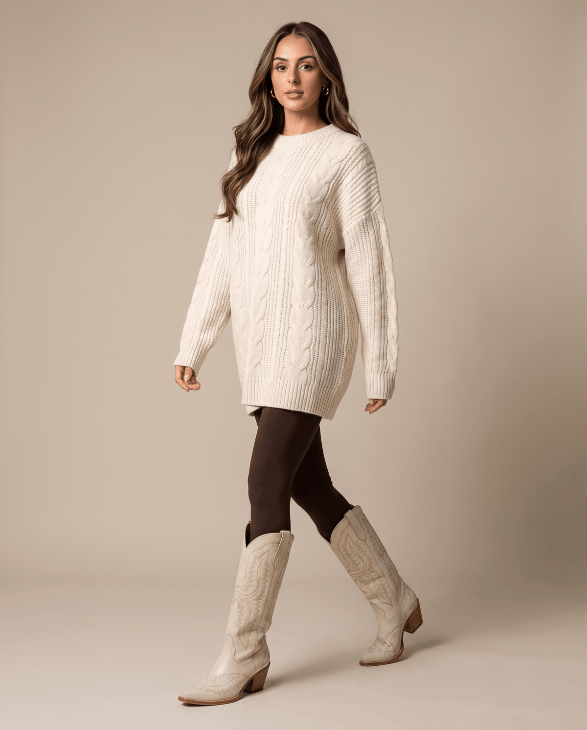 Woman in an oversized cream sweater and brown tights wearing cream western boots