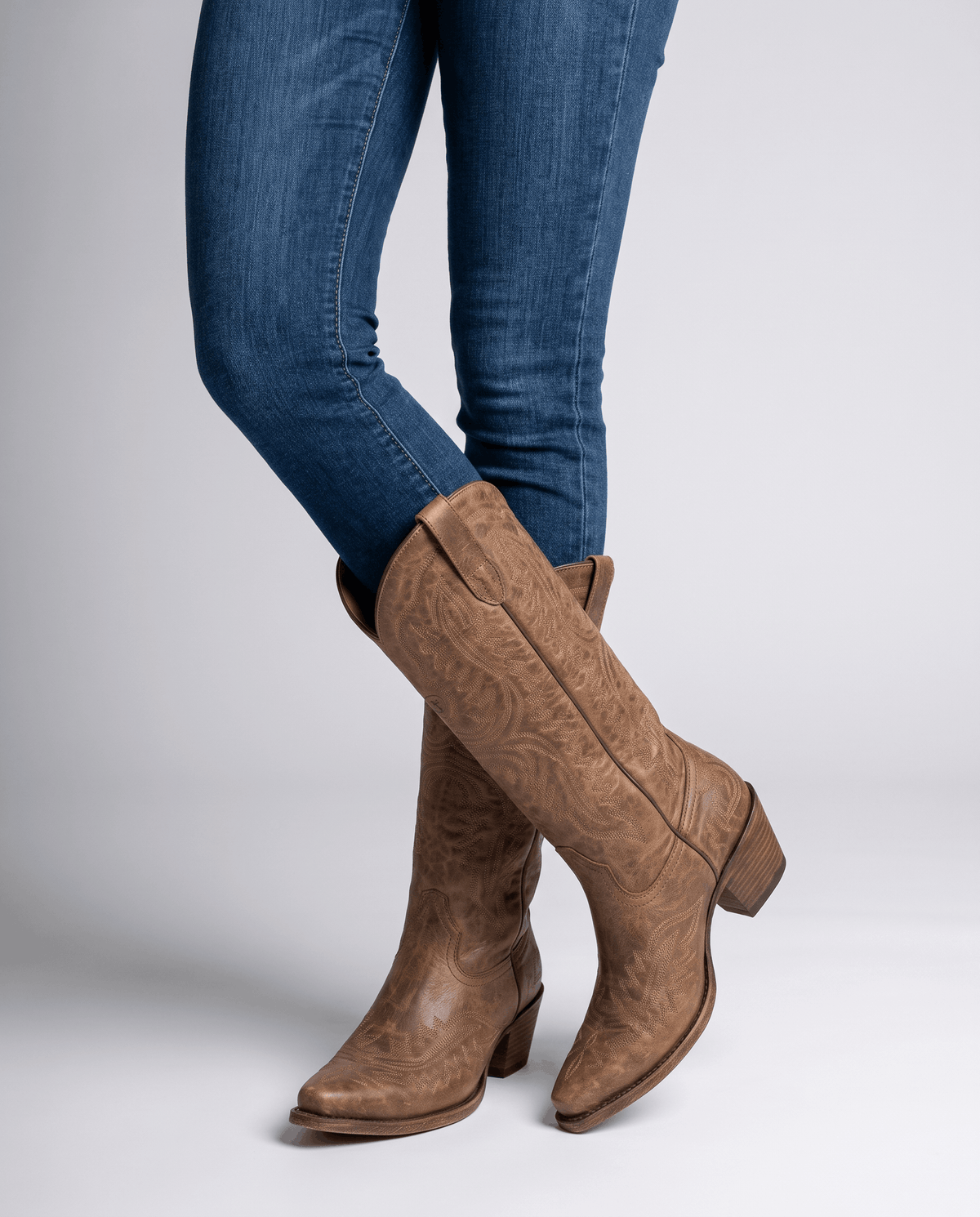 Model standing in blue skinny jeans tucked into dark brown embroidered boots