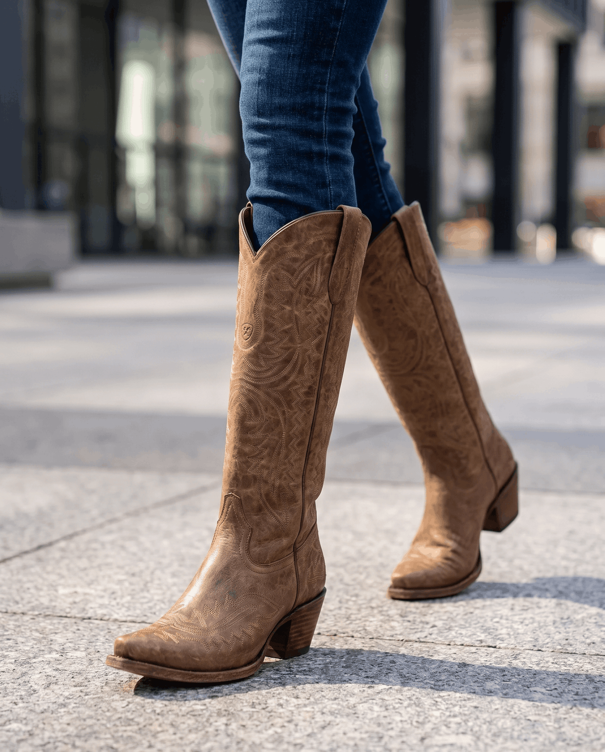 Walking on a city sidewalk in dark brown western boots and tucked blue jeans