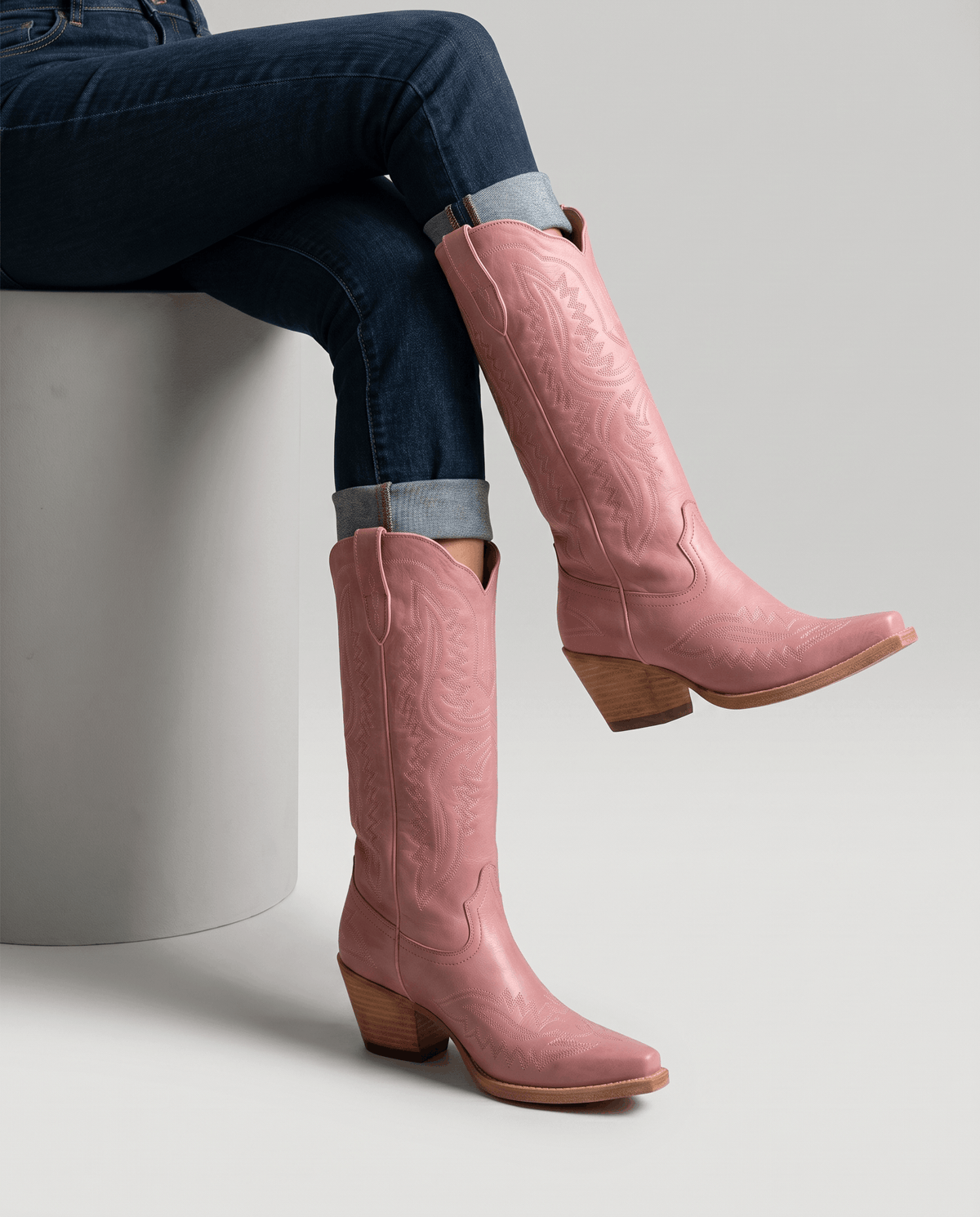 Seated model in cuffed jeans wearing pink mid-calf boots with stacked heels