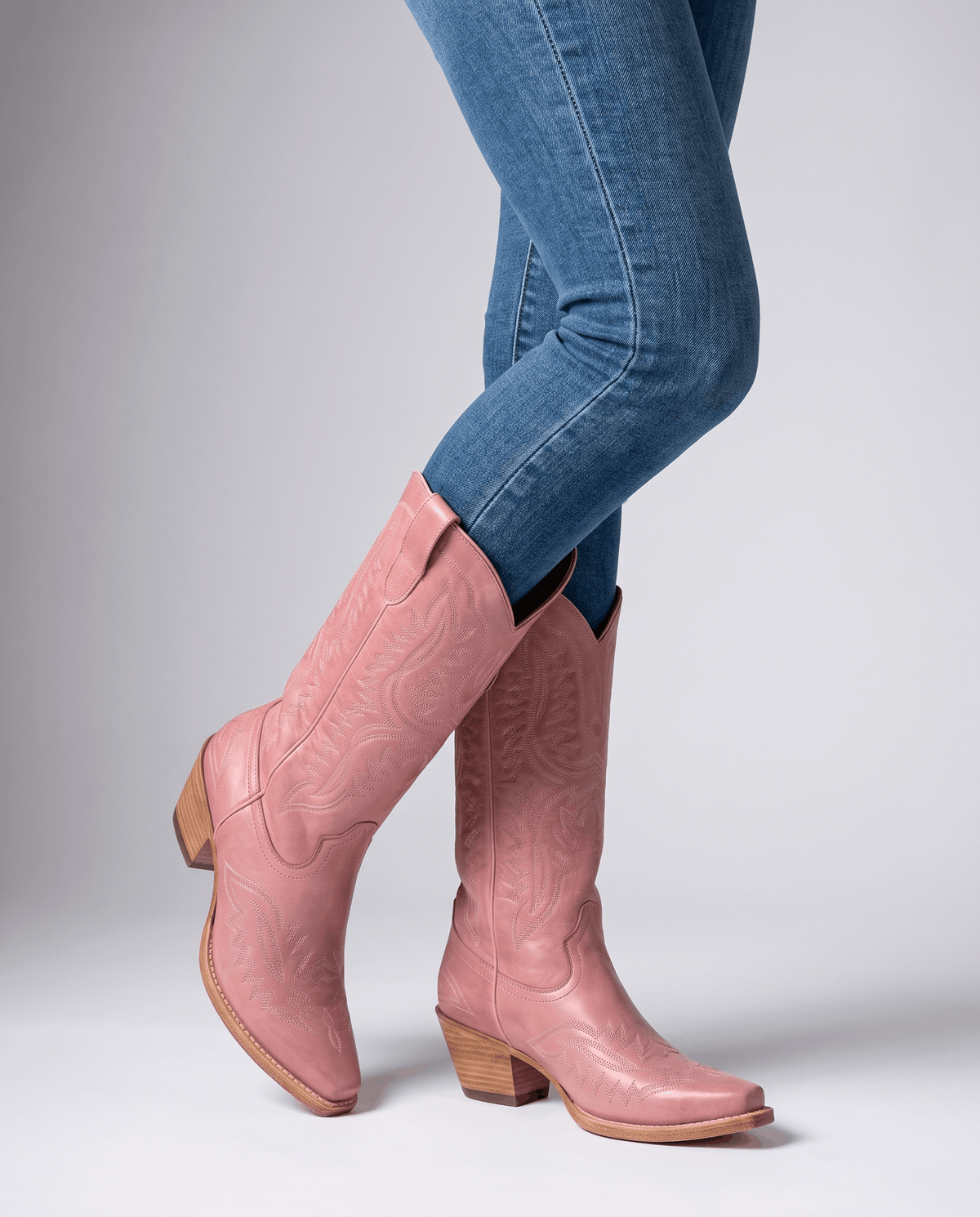 Pink embroidered boots mid-stride with blue jeans tucked into the shaft