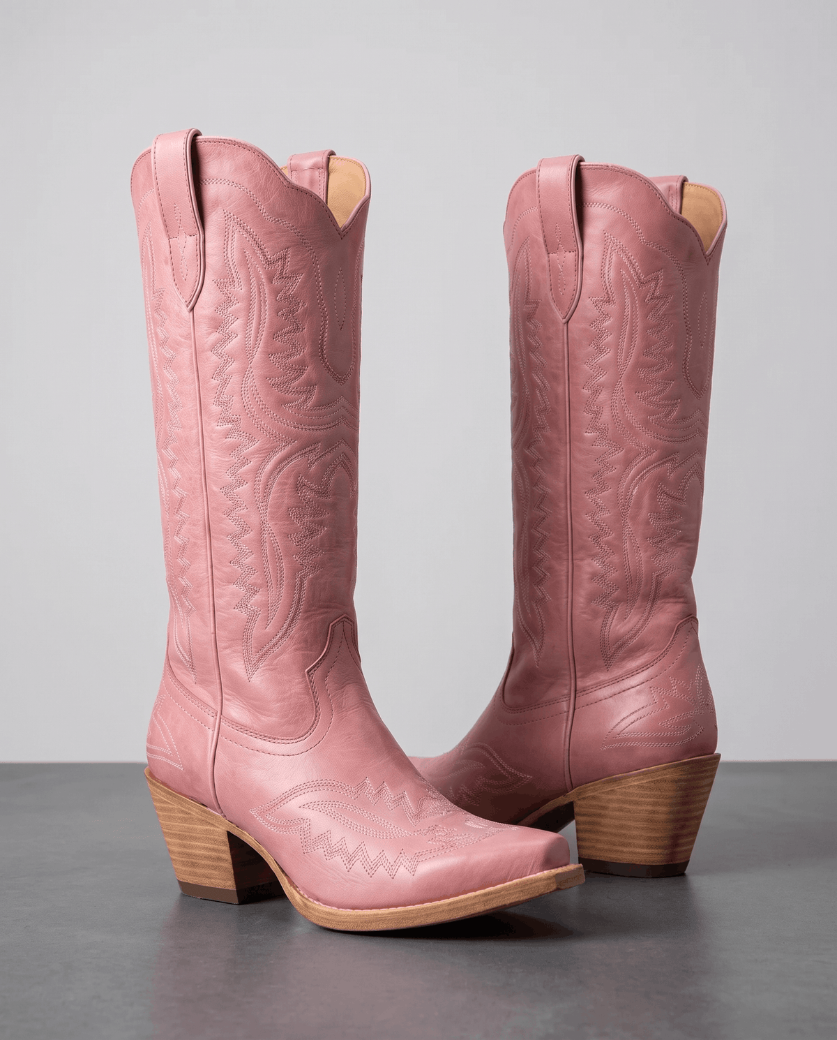 Pair of pink embroidered cowboy boots with pointed toes on a grey studio floor