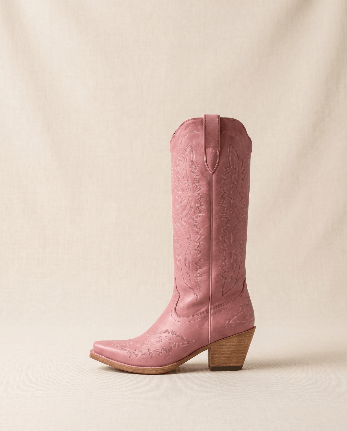 Single pink western boot in side profile against a warm beige backdrop