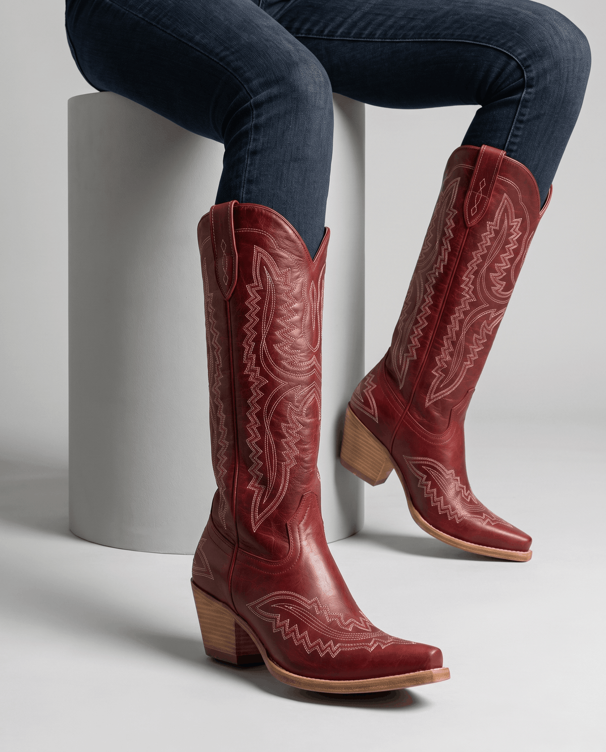 Seated model wearing red embroidered boots with blue jeans tucked inside