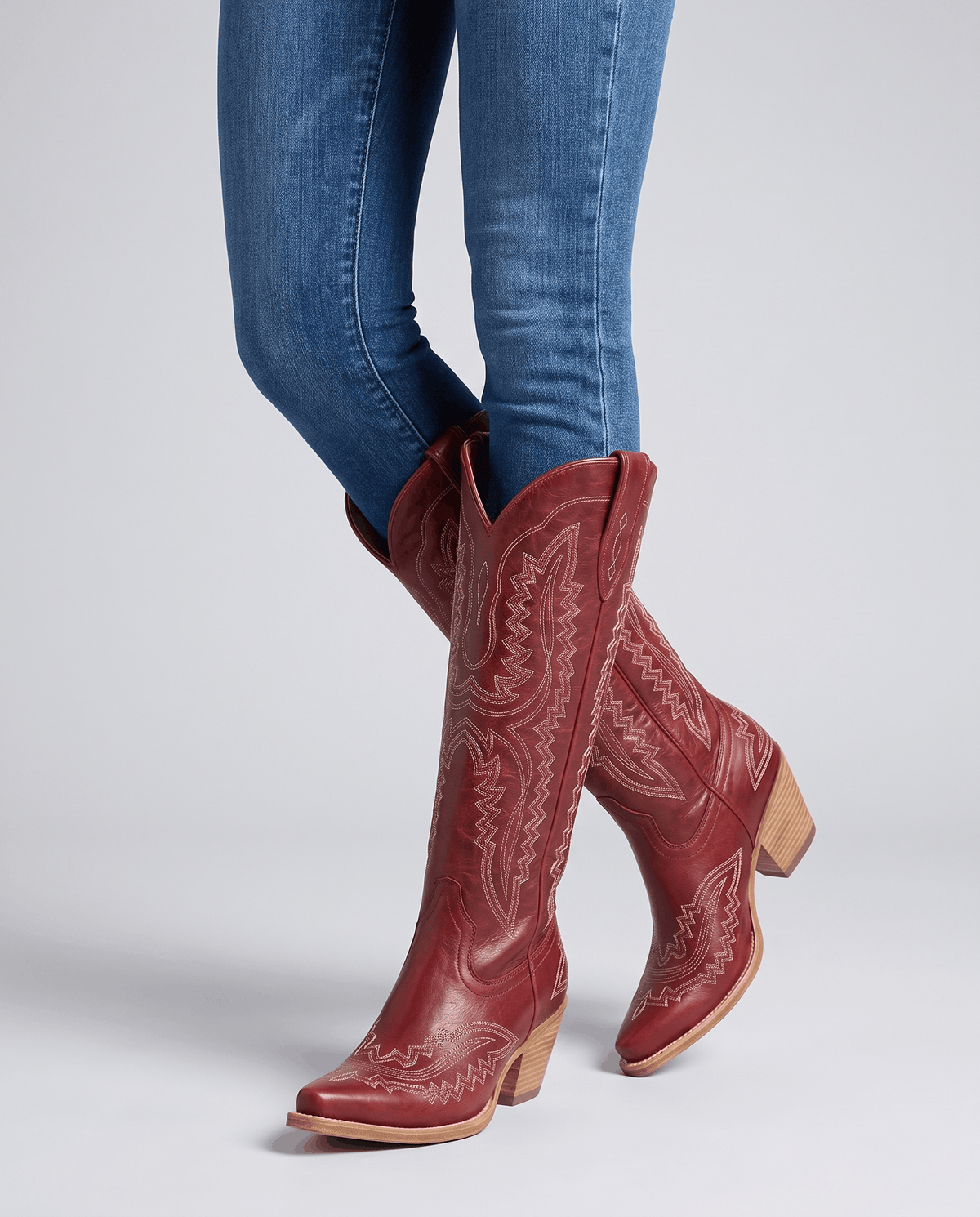 Close view of red mid-calf boots worn standing with tucked skinny jeans