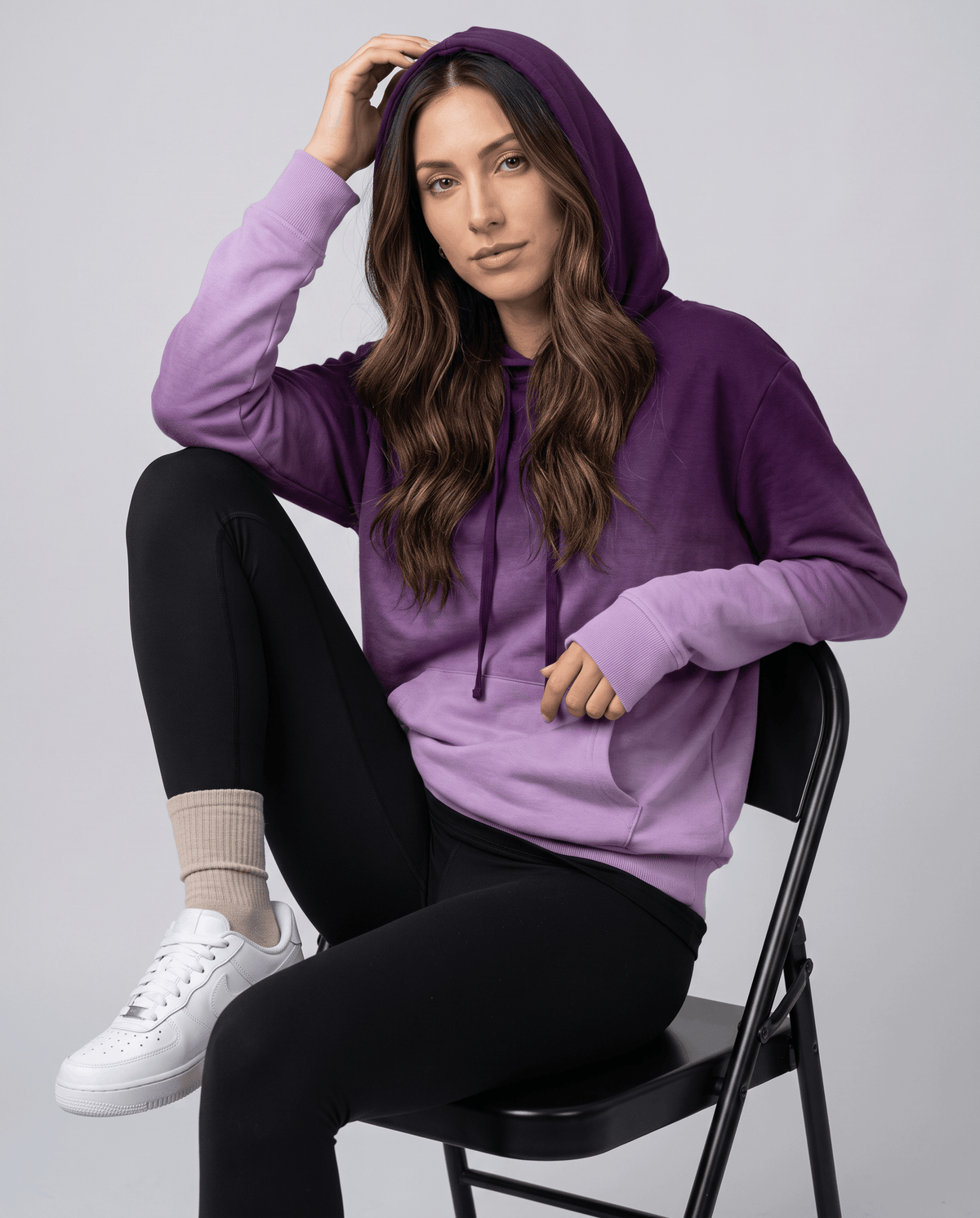 Seated look in the purple fade hoodie with hood up, black leggings and white sneakers