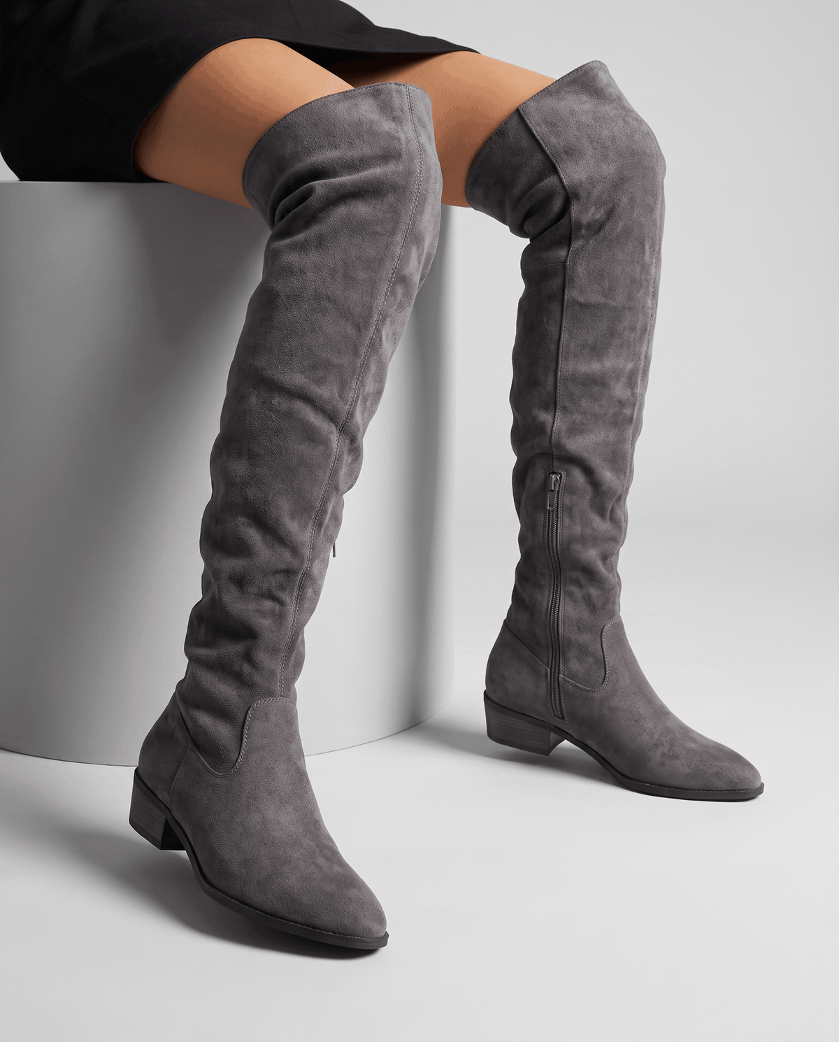Seated woman in a black skirt wearing gray suede boots above the knee