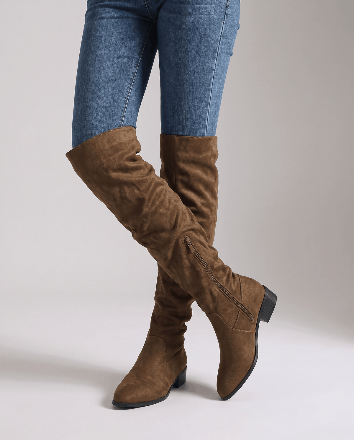 Woman in blue jeans walking in olive brown boots that cover the knee