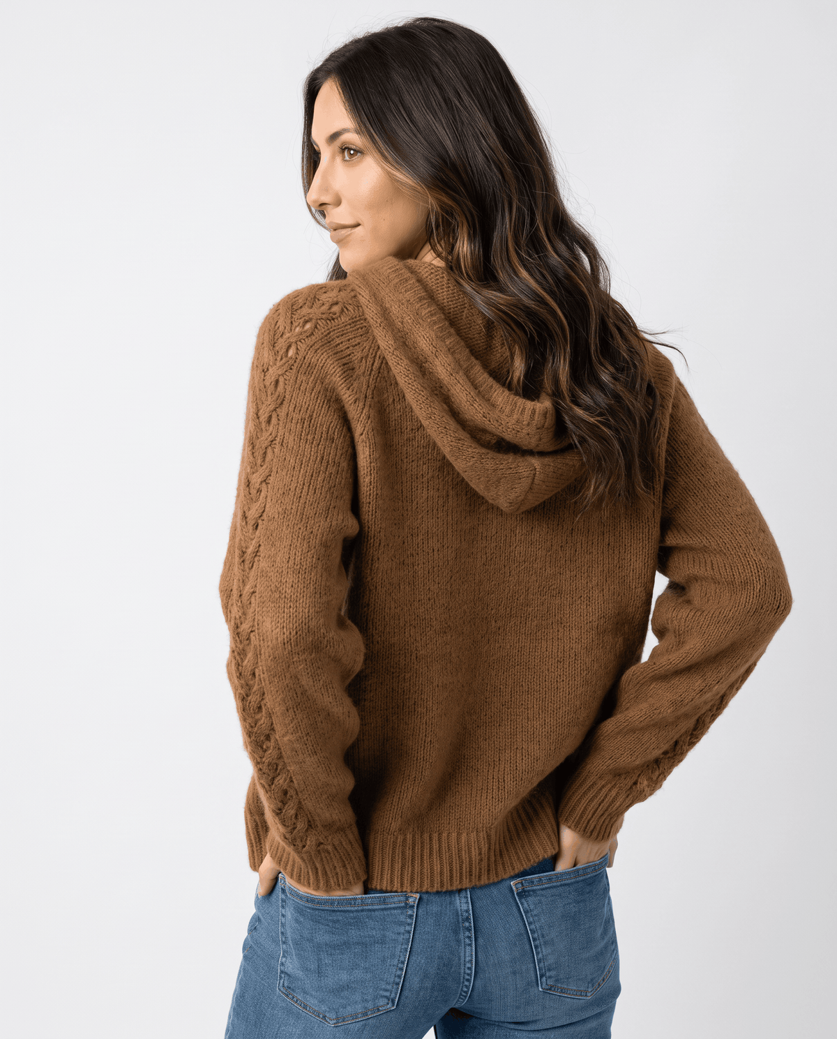 Back angle of the brown knit sweater showing the hood and relaxed sleeves with jeans