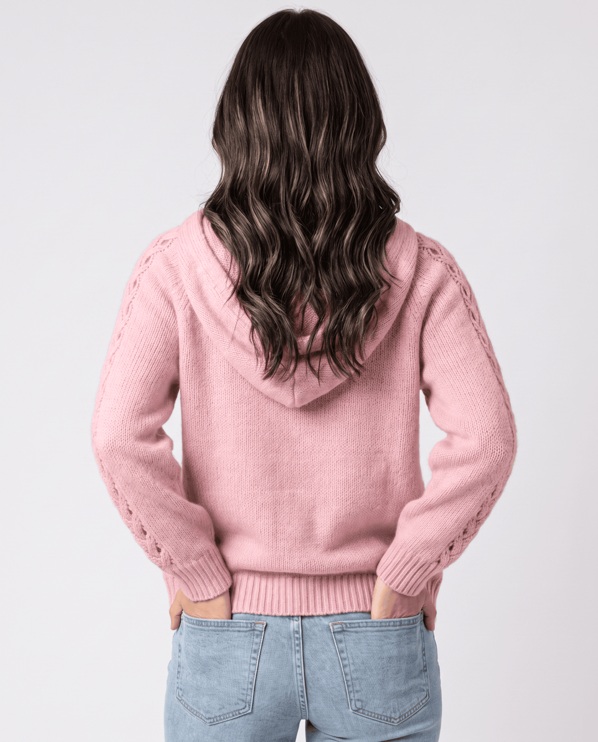 Back view of the pink knit sweater with the hood resting over jeans