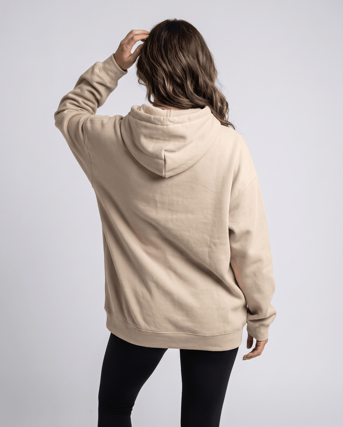 Back view of the khaki loose-fit hoodie with the hood down over black pants