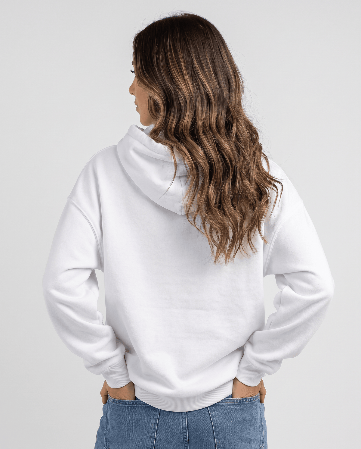 Back view of the white loose-fit hoodie with the hood down over jeans