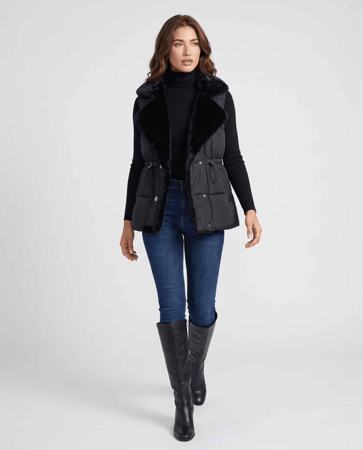 Full-length look with black padded vest, blue jeans and tall black boots