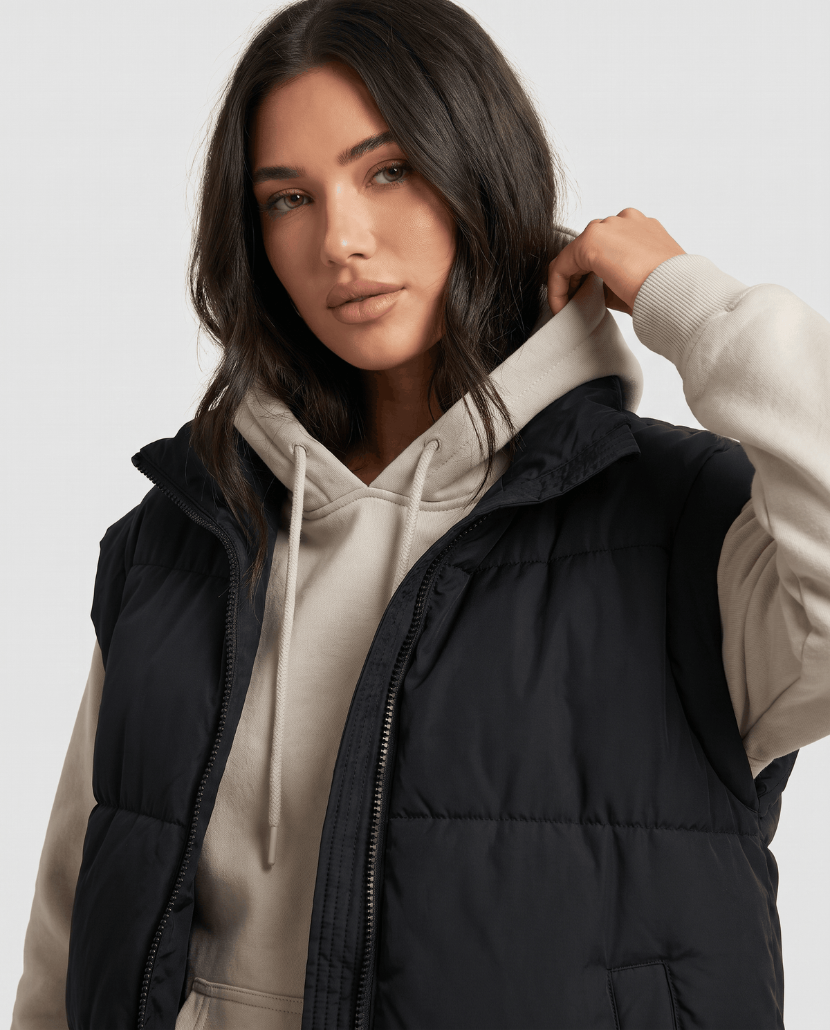 Black padded vest zip front and stand collar worn over a beige hoodie
