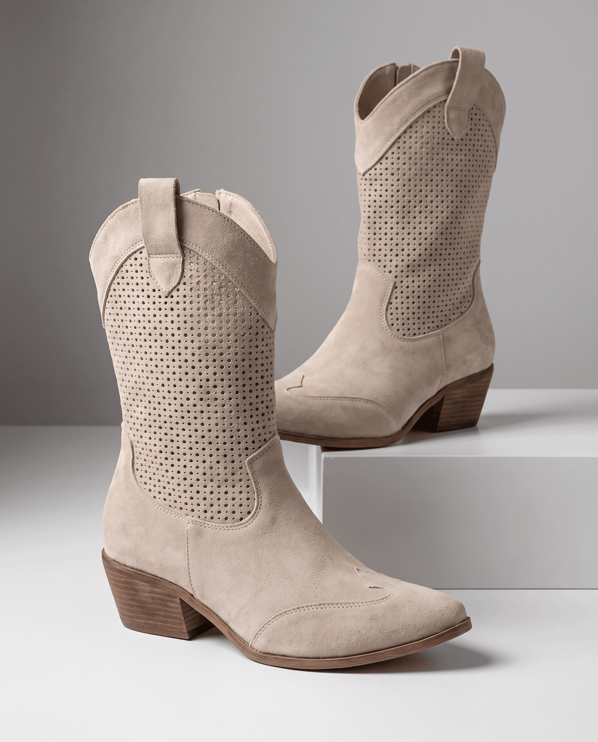 Pair of beige perforated western boots displayed on a white pedestal