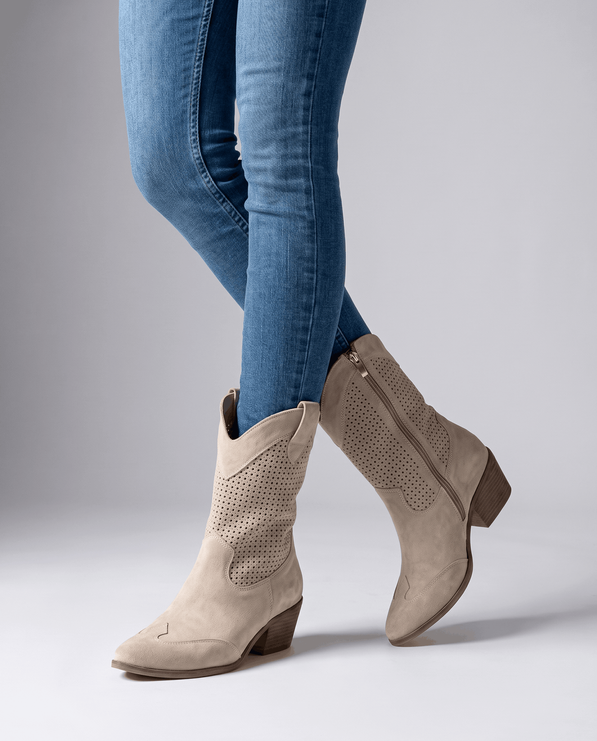 Beige cut-out cowboy boots worn standing with blue skinny jeans tucked in